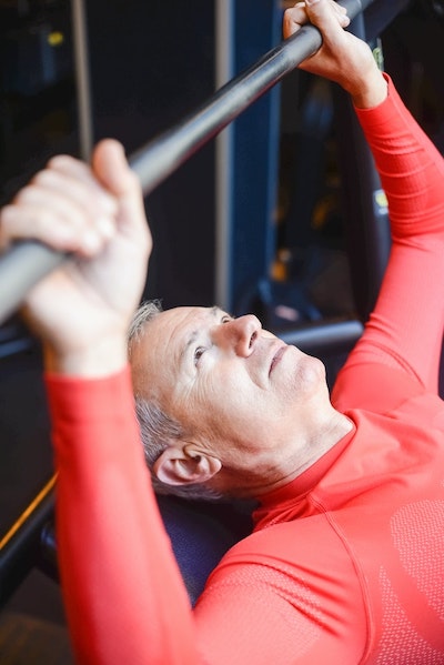 An older man performs a bench press with a barbell to improve strength